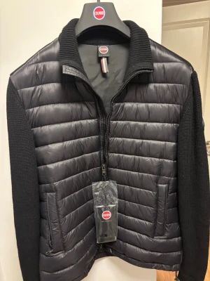 Svart cardigan från Colmar - Snygg svart hybridjacka/cardigan från Colmar med quiltad front och släta stickade ärmar. Jackan har hög krage, dragkedja framtill och två sidofickor. Materialmix med glansig nylon på kroppen och stickat tyg på ärmar och krage ger en modern look. Perfekt nu till våren.