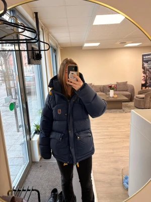 Mörkblå dunjacka från Fjällräven - Säljer min fjällräven jacka då jag har köpt ny, älskar denna jacka den är jättevarm, snygg och perfekt för kalla dagar. Den har en skada på armen som jag har lagat med en lapp köpt från fjällrävens hemsida, skriv för fler bilder 