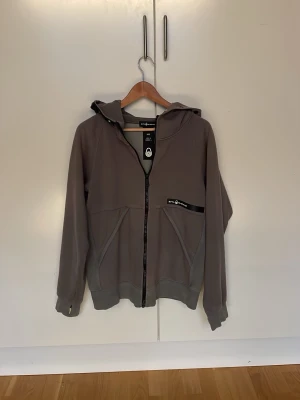 Grå hoodie från Peak Performance - Snygg grå hoodie från Sail racing med dragkedja framtill och två stora fickor. Tröjan har en huva med svart kant och diskret logga på både huva och bröst. Tillverkad i mjukt material som känns skönt mot huden. Perfekt för en avslappnad stil. Nypris 1800 kr Hör av er vid minsta fundering mvh Artur