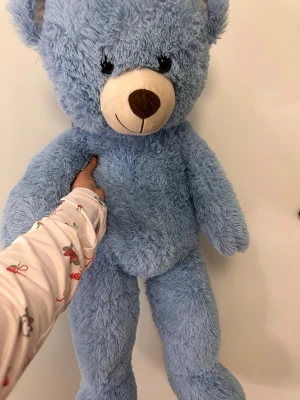 Stor blå nallebjörn mjukisdjur - Säljer en stor och fluffig nallebjörn i ljusblått plyschmaterial. Nallen har ett runt ansikte med vit nos, bruna detaljer och svarta ögon. Perfekt som mysig inredningsdetalj eller present till någon du gillar.