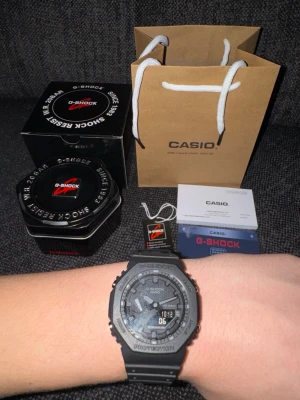 Svart Casio G-Shock digital klocka - Säljer en svart Casio G-Shock klocka med digital och analog display. Klockan har robust design, resinarmband och klassisk G-Shock-logga. Kommer med originalförpackning, manual och garanti. Perfekt för dig som gillar sportig och tålig stil.