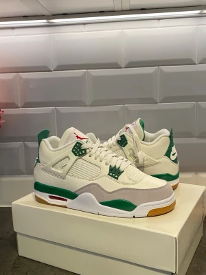 Nike SB Air Jordan 4 Retro vit/grön - Nike SB Air Jordan 4 Retro sneakers i vitt och grönt med detaljer i grått och gult. Skorna har meshpaneler, mockadetaljer och klassisk Jordan-logga på plösen. Tjock sula med synlig Air-enhet och Nike SB branding på hälen. Perfekt för dig som gillar streetwear och unika sneakers.