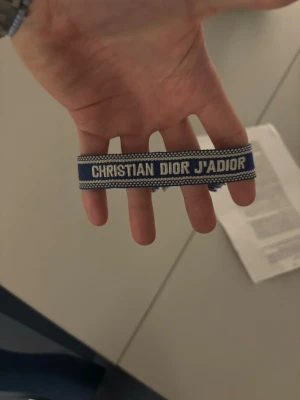 Blått Christian Dior tyg armband - Snyggt blått tygarmband från Christian Dior. Armbandet har en vävd design med vita detaljer längs kanterna och känns både trendigt och exklusivt. Perfekt accessoar för att lyfta din outfit med en lyxig touch. Armbandet är köpt på dior i spanien, kvittot är borttappat därav kan priset diskuteras. Är öppen för alla förslag och ibland byten beroende på vad det är! Tveka inte på att höra av dig