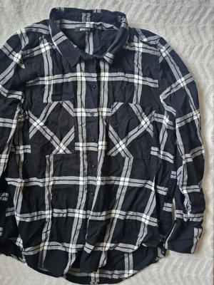 Svartvit rutig skjorta Gina Tricot - Säljer en svart skjorta från Gina Tricot med vitt rutmönster. Skjortan har klassisk krage, knäppning framtill och två bröstfickor. Långärmad modell i mjukt tyg, perfekt för en avslappnad look.