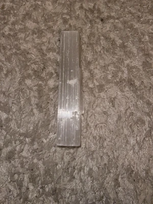 Selenitstav kristallvit - En avlång, kristallvit selenitstav med naturliga linjer och en slät yta. Perfekt som dekoration, för kristallsamling eller spirituella ändamål. Staven är genomskinlig med en lätt glans och har en rektangulär form.