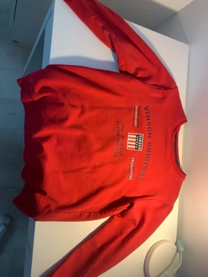 Röd sweatshirt från Vinson - Cool röd sweatshirt från Vinson med tryck på bröstet och rund hals. Tröjan har långa ärmar och ribbade muddar vid hals, ärmslut och nederkant. Perfekt för dig som gillar en sportig och avslappnad stil.