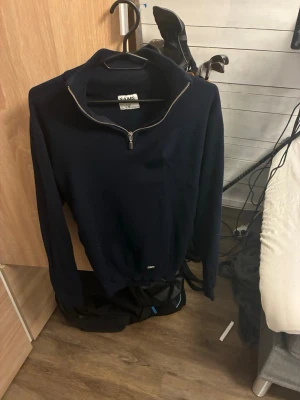Mörkblå halvzip från SAMS - Mörkblå tröja från SAMS med halv dragkedja och hög krage. Tröjan har långa ärmar och en enkel, stilren design som passar perfekt till jeans eller chinos. Tillverkad i mjukt material för extra komfort.