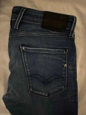 Mörkblå Replay jeans  - Snygga mörkblå jeans från Replay med raka ben och klassisk femficksmodell. Jeansen har slitningar och ljusare partier för en trendig look samt Replay-logga på bakfickan. Tillverkade i mjuk denim med kontrastsömmar.