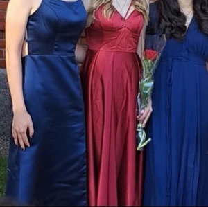 Marinblå långklänning JJ's House - Snygg marinblå långklänning från JJ's House med smala axelband och snörning i ryggen. Klänningen har en elegant, figurnära passform upptill och faller snyggt nedåt. Tillverkad i glansigt satinliknande material som ger en lyxig känsla. Köpte klänninge ny för 1300kr och har används en gång. Jag är 173 cm och kunde inte ha klackar så perfekt för personer som är kortare än 173. 