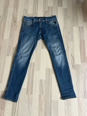 Blå slim fit jeans från Replay 30/30 - Snygga blå slim fit jeans från Replay med klassisk femficksdesign och en tvättad stil. Jeansen har normal midja, smala ben och kontrastsömmar. Perfekta för en avslappnad och trendig look.