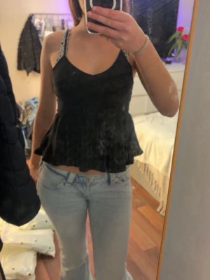 Svart volangig linnetopp - Säljer en svart linnetopp med smala axelband och v-ringning. Toppen har en volangig nederdel som ger en flowy känsla och är perfekt för att styla med jeans eller kjol. Enkel men snygg design som passar till många olika looks.