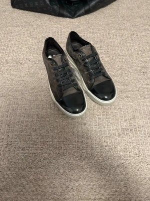 Lanvin Cap Toe Gråa (helt nya) - Snygga gråa lanvins med glansig tå och klassiskt monogrammönster på sidan. Skorna har svarta skosnören och vit sula. Materialmix av läder och textil ger en exklusiv känsla och modern look.