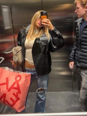 Svart oversized skinnjacka - Snygg svart oversized skinnjacka med bred krage och stora fickor framtill. Jackan har en avslappnad passform och trendig look som passar perfekt till jeans och crop top. Perfekt för dig som vill ha en cool och modern stil.
