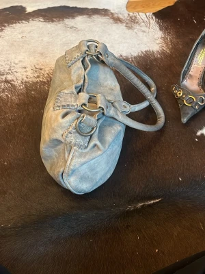 Grå handväska i mjukt äkta skinn med ”gammelguldiga” detaljer. 32 cm på bredden, 28 cm på längden, skriv för mer frågor☺️ - Säljer en blå handväska i mjukt skinn med dubbla handtag och snygga metallringar som detaljer. Väskan har en avslappnad, lite slouchy form och dekorativa sömmar vid handtagen. Perfekt för dig som gillar en cool och casual look.