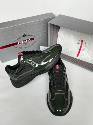 Mörkgröna sneakers från Prada - Snygga mörkgröna sneakers från Prada med glansig finish och svarta meshdetaljer. Skorna har svarta snören, svart sula och en röd Prada-logga på plösen. Materialmix av lack och mesh ger en modern och exklusiv känsla.