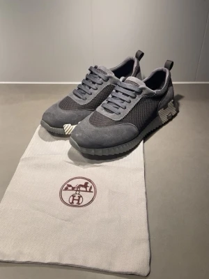 Grå skor H - Snygga grå sneakers  med ovandel i mocka och mesh. Skorna har en chunky sula i gummi med unika detaljer på sidan och klassiska snören. Perfekt för dig som gillar exklusiva och stilrena sneakers med modern touch.
