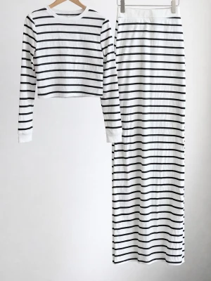 Randigt set från SHEIN, långärmad & kjol - Säljer ett snyggt tvådelat set från SHEIN med svartvita horisontella ränder. Setet består av en långärmad crop top och en lång, rak kjol. Materialet är mjukt och stretchigt, perfekt för en trendig look. Storlek L (EU 40/42).