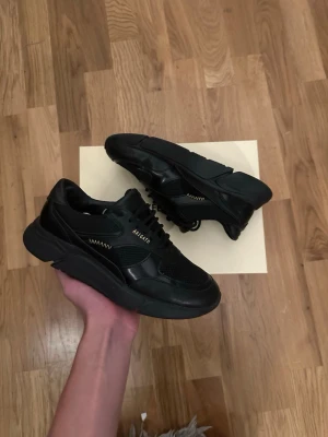 Svarta sneakers Axel Arigato - Snygga svarta sneakers från Axel Arigato med chunky sula och meshdetaljer. Skorna har en modern design med blandning av läder och textil, samt diskret logga på sidan. Perfekta för dig som gillar stilrena och trendiga sneakers. Använda ett fåtal gånger! Skolådan kommer med!