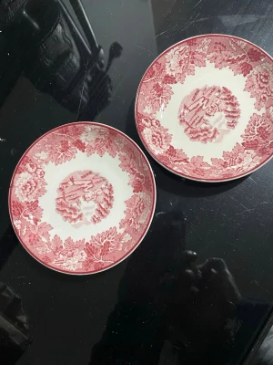 Två assietter Woods Ware English Scenery fat - Två fina assietter från Woods Ware English Scenery fat med klassiskt rödblommigt mönster. Tallrikarna är vita med detaljer i rött och har ett dekorativt blommotiv runt kanten. Perfekta till fika eller som dekoration i köket.