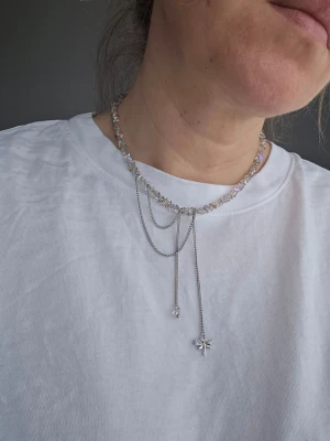 Silverfärgat halsband med pärlor och hänge - Unikt halsband i silverfärg med skimrande pärlor och flera tunna kedjor. Halsbandet har ett dekorativt hänge och små gnistrande detaljer som ger en cool och trendig look. Perfekt för dig som gillar att sticka ut med accessoarer.