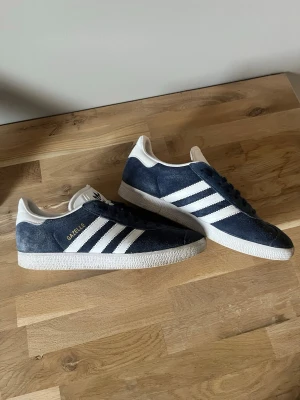 Adidas Gazelle Skor - Mörkblå Adidas Gazelle sneakers till säljes för billigt pris. De är i bra skick men kan visa små tecken på användning, exempelvis på plösen. De är i storlek 40 2/3 och är perfekt för vår och sommar. Hör av er om minsta fundering💫