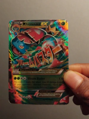 Pokémonkort Mega Venusaur EX - Unikt Pokémonkort med Mega Venusaur EX, holografisk yta och japansk text. Kortet har färgstarka detaljer i grönt, blått och rött samt coolt motiv av Venusaur. Perfekt för dig som samlar eller gillar Pokémonkort och vill ha något extra i din samling.