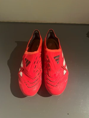 Adidas Predator röda fotbollsskor - Skriv om du har några frågor så svarar jag så snabbt som möjligt! Nypris: 3249kr unisport. Säljer ett par Adidas Predator fotbollsskor i rött med vita och svarta detaljer. Skorna har klassisk låg profil, snörning och dobbar för spel på gräs. Tillverkade i syntetmaterial för bra grepp och kontroll på planen. Perfekta för dig som vill sticka ut på matchen.
