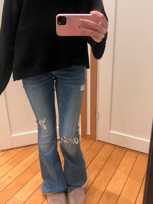 Blå lowwaist bootcut jeans från Gina Tricot som väntar på dig (endast använda en gång!) - Säljer ett par helt nya blå bootcut jeans från Gina Tricot i storlek XS. Jeansen har slitna detaljer vid knäna och låret, klassisk femficksmodell och normalhög midja. Tillverkade i denim med snygg tvätt och råa kanter vid slitningarna. En ny familjemedlem till din garderob 