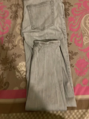 Ljusgrå raka jeans - Säljer ett par ljusgrå jeans med raka ben och klassisk femficksdesign. Jeansen har en enkel look utan slitningar eller dekorationer och är tillverkade i ett mjukt denimtyg. Perfekta för en avslappnad och stilren outfit.