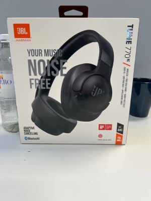 JBL Tune 770NC trådlösa hörlurar - Säljer ett par svarta JBL Tune 770NC over-ear hörlurar med adaptiv brusreducering och Bluetooth. Hörlurarna har en stilren design och är tillverkade i plast med mjuka öronkuddar för extra komfort. Perfekta för musik och poddar med lång batteritid.