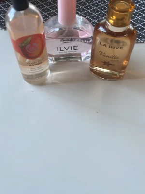 Tre parfymer: Mango, Ilvie, Vanilla - Säljer tre olika parfymer: en med mangodoft i genomskinlig flaska med orange etikett, en Ilvie Eau de Parfum i rosa och genomskinlig flaska samt en La Rive Vanilla i bärnstensfärgad flaska med guldkork. Perfekt för dig som gillar fruktiga och söta dofter.