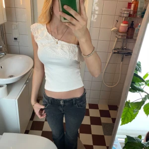 Vit oneshoulder topp med spetsdetaljer - Säljer en superfin vit oneshoulder topp med spetsdetaljer. Den är tight och perfekt för sommaren. Toppen har en unik design med volang och spets från kappahl, endast använd 2 gånger☀️