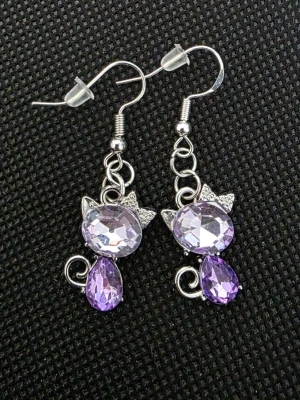 Lila kattörhängen med strass - Söta örhängen i form av katter med gnistrande lila och ljuslila stenar. Örhängena har silvrig metall, små öron och svansdetaljer. Perfekt accessoar för dig som gillar djur och vill sticka ut med något unikt.