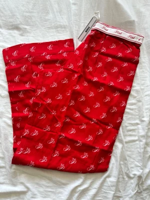 Röda pyjamasbyxor från Pink - Snygga röda pyjamasbyxor från Pink med vitt mönster och elastisk midja med logotyp. Byxorna har ett avslappnat snitt och är perfekta för chill dagar hemma. Tillverkade i mjukt material för extra komfort.