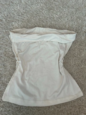 Vit bandeau tubtopp - Säljer en enkel och stilren vit bandeau tubtopp. Toppen är axelbandslös och har en bred kant upptill som ger en snygg passform. Perfekt att matcha med jeans eller kjol för en clean look.