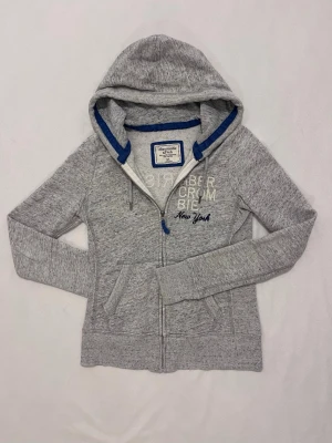 Abercrombie & Fitch Zip Hoodie - Grå hoodie från Abercrombie & Fitch med text på ryggen                       Ganska bra skick                                Säljer för att jag inte använder den mer                            
