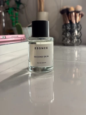 ESSNCE Second Skin Eau de Parfum - Minimalistisk parfymflaska från ESSNCE med doften Second Skin. Flaskan är genomskinlig med svart lock och vit etikett med svart text. Modern och stilren design som passar perfekt på sminkbordet.                      OBS! kan ej skicka mellan 20 juli till 19 augusti 