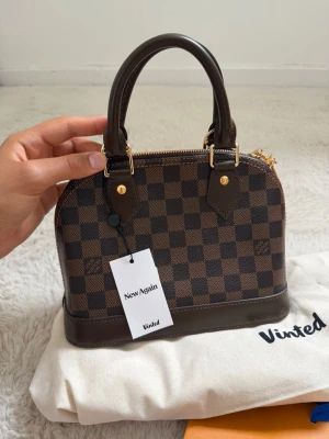 Louis Vuitton Alma BB Damier väska  - Mycket snygg Alma BB damier handväska från Louis Vuitton, den är i galant skick och tillkommer med kvitto samt annat. Köpt på vinted samt verifierad av de som ni ser på intyget.