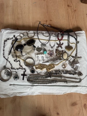 Stort smyckespaket med vintage, Y2K och statement-smycken! 💍✨ - Säljer ett stort paket med blandade smycken och accessoarer. Innehåller halsband, armband, örhängen, broscher, ringar och solglasögon i olika färger som silver, guld och svart. Flera smycken har detaljer som stenar, hjärtan, fjärilar och kors. Perfekt för dig som gillar att mixa stilar!Kommer budas ut på min live 15 juli 19.00.