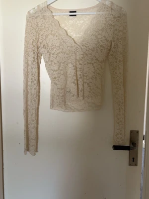 Beige spetsblus från Gina Tricot - Säljer en beige långärmad spetsblus från Gina Tricot. Blusen har v-ringning med vågig kant och är helt täckt av ett blommigt spetsmönster. Perfekt för dig som gillar romantiska detaljer och en feminin look.