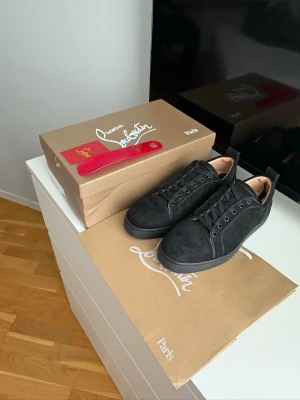 Svarta sneakers från Christian Louboutin - Stilrena svarta sneakers från Christian Louboutin i mocka med klassisk låg profil och svarta skosnören. Skorna har diskreta detaljer och en svart sula som ger en clean look. Perfekta för dig som gillar exklusiva och tidlösa sneakers.