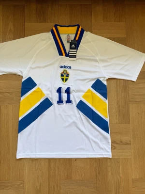 Brolin #11 – Sverige 1994 Borta (storlek M) - Brolin #11-tryck. Sverige 1994 Borta (vit). Storlek M. Helt ny och aldrig använd. Skickas snabbt 🚚💨  Mått (M): Halvt bröstmått 53 cm • Längd 74 cm • Ärmbredd 23 cm • Axelbredd 44 cm • Ärmlängd 40 cm • Manschett 19 cm.  🔥 Fan Edition – normal passform. 🇸🇪 Sverige landslag.  📩 Skicka gärna ett meddelande vid frågor eller prisförslag! 🛍 Bundle-rabatt upp till 20%! 📦 Skickas samma eller nästa dag.