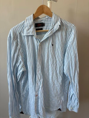 Morris Stockholm Pure Linen Shirt - Classic Fit - * Märke: Morris Stockholm * Modell: Classic Fit * Material: 100 % lin (Pure Linen) * Storlek: M (39/40) * Färg: Ljusblå/vit randig                                                  * Nypris 1499 kr