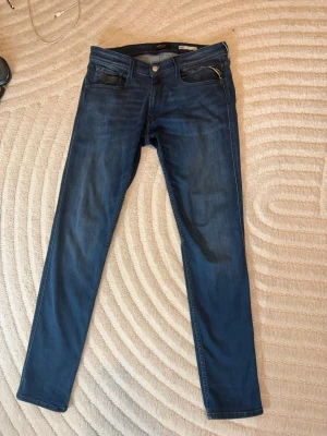 Mörkblå slim fit jeans Replay - Snygga mörkblå jeans från Replay i modellen Anbass med slim fit. Klassisk femficksdesign, silverfärgade detaljer och diskret logga på fickan. Perfekta för dig som gillar en smalare passform och stilren look.