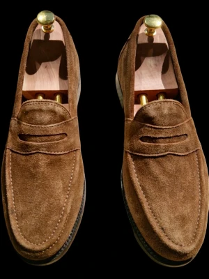 Bruna mocka loafers Samuel Windsor  - Snygga loafers i brun mocka med klassiskt pennyband över vristen ifrån Samuel Windsor. Skorna tillverkade i Gooyyear konstruktion har en rundad tå och diskreta sömmar som ger en stilren look. Perfekta för dig som gillar tidlös och avslappnad stil. Yttermaterialet är mjukt och ger en lyxig känsla. I Storlek 9UK vilket motsvarar 43. 