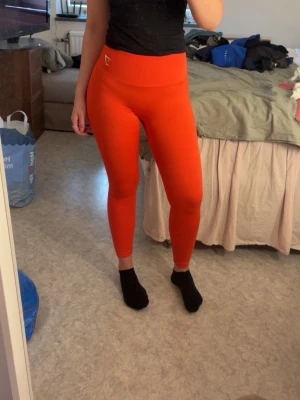 Röda seamless tights från Gymshark - Säljer ett par röda seamless tights från Gymshark med hög midja och tight passform. Materialet är stretchigt och följsamt, perfekt för träning eller chill. Diskret logga framtill i vitt. Supersnygga och bekväma leggings som sitter på plats under hela passet.