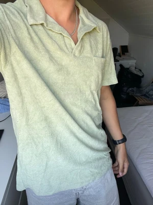Ljusgrön frotté polotopp M - Säljer en ljusgrön polotopp i mjuk frotté med klassisk krage och bröstficka. Perfekt för dig som gillar avslappnad stil och vill ha något bekvämt men ändå snyggt. Passar till både jeans och shorts.
