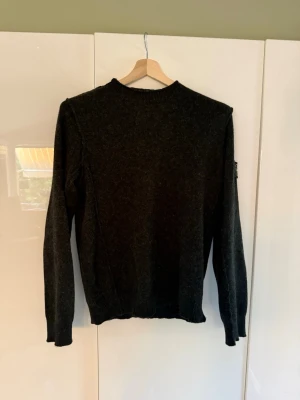 Stickad Tröja Stone Island - Säljer en Stone Island stickad tröja i svart/grön, storlek M  Tröjan är i bra använt skick och har den klassiska Stone Island-kompasspatchen på vänster ärm. Ett stilrent och tidlöst plagg som passar året runt.