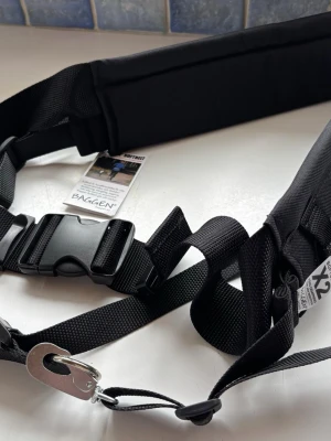 Baggen Softbelt X2 hundbälte svart - Baggen Softbelt X2 är ett svart midjebälte i slitstarkt nylon med hård dämpning, perfekt för hundpromenader eller löpning. Bältet har snabbspänne, vadderad sektion och metallkrok för koppel. Märkt med Baggen Umeå, Sweden.