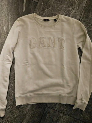 Vit  sweatshirt från GANT - Snygg vit sweatshirt från GANT med broderad logga framtill. Tröjan har rund halsringning, långa ärmar och ribbade muddar vid ärmslut och nederkant. Perfekt för en avslappnad och stilren look.